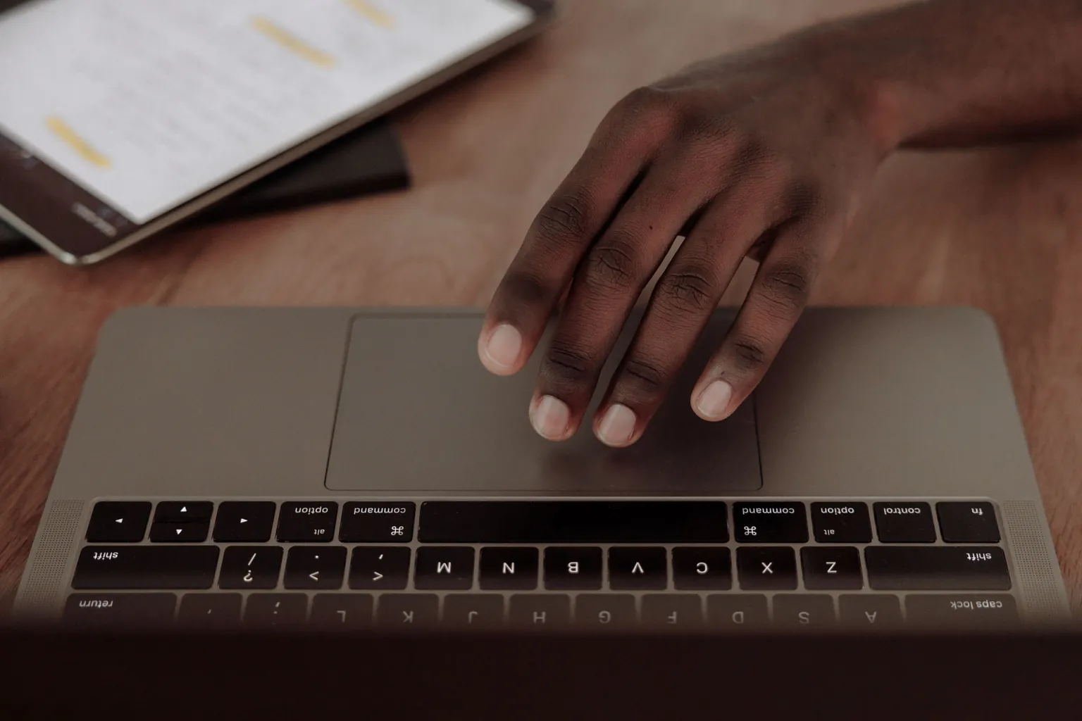 Main posée sur le pavé tactile d'un ordinateur portable, une tablette à côté