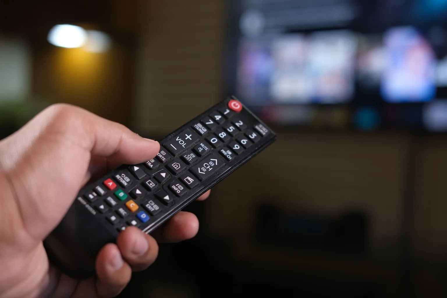 Main tenant une télécommande devant un écran de télévision flou
