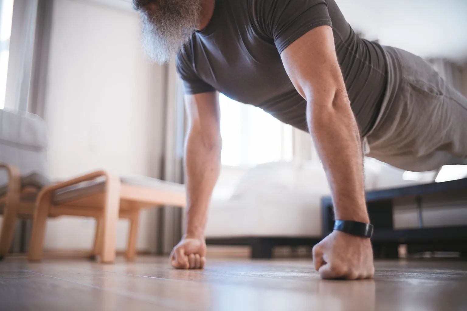 Homme barbu en tee-shirt gris faisant une pompe sur les poings dans son salon