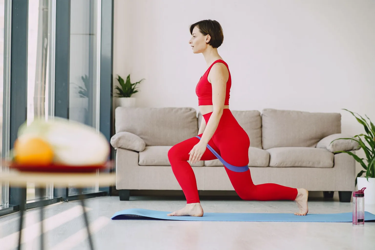 Femme en tenue rouge en position de fente sur un tapis dans un salon, un élastique autour des cuisses