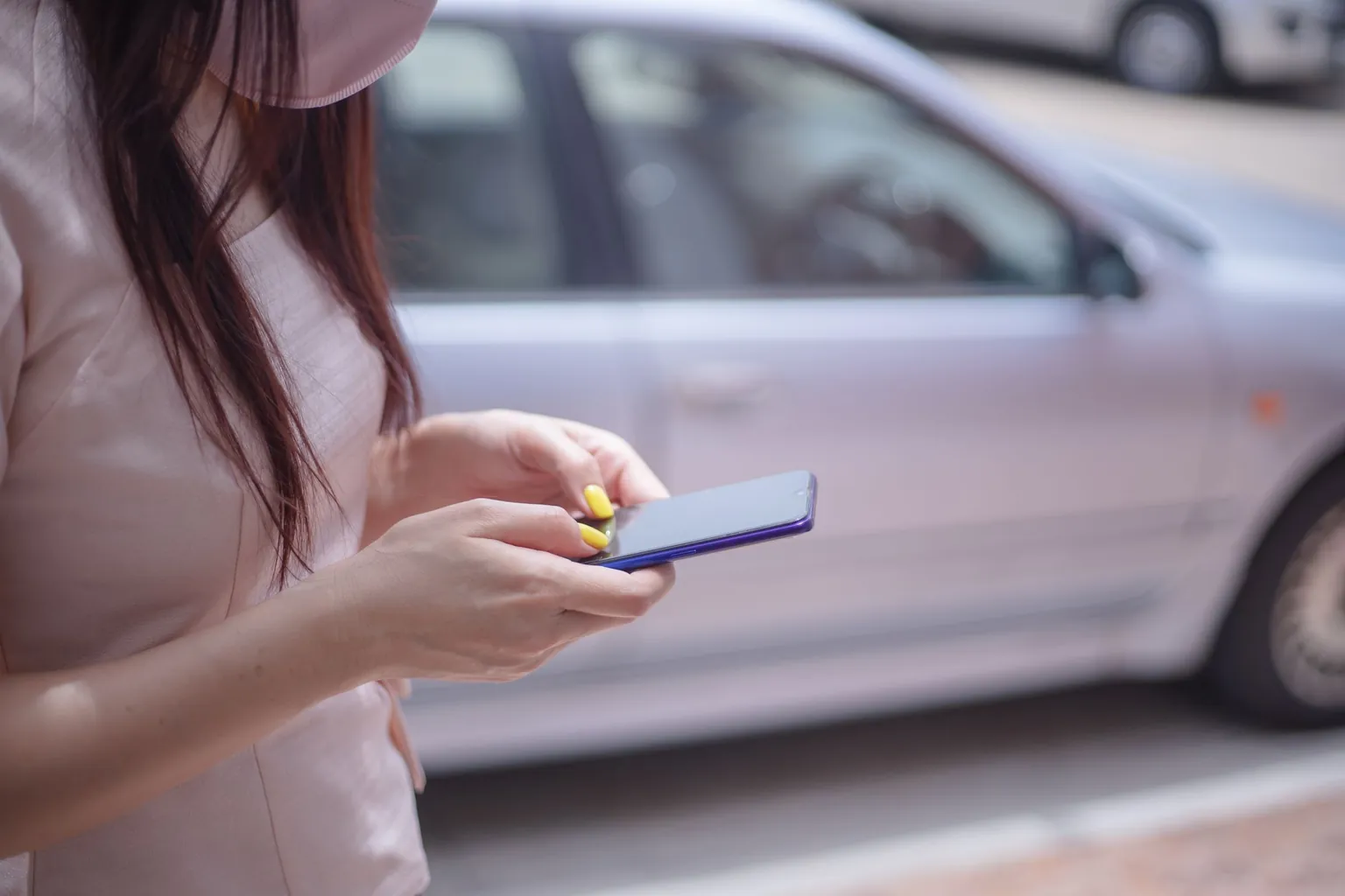 Une femme consulte son smartphone sur un trottoir, devant une voiture garée