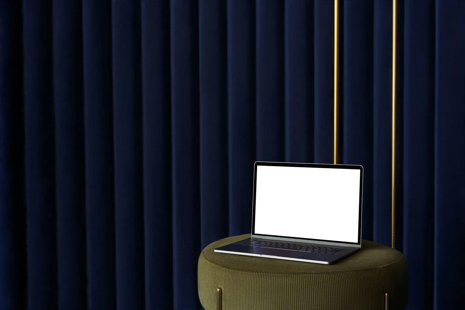 Ordinateur portable ouvert, écran blanc allumé, posé sur un pouf vert devant un rideau bleu nuit